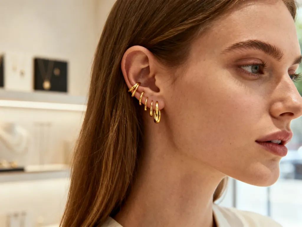 Zbliżenie na ucho kobiety ozdobione wieloma eleganckimi złotymi kolczykami w nowoczesnym butiku jubilerskim.