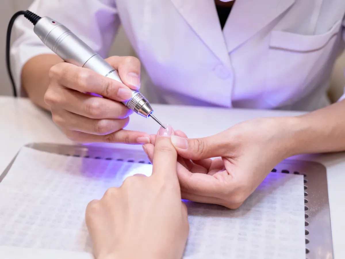 Stylistka ostrożnie usuwa twardą bazę frezarką w salonie
